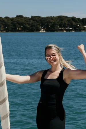 Manuela Nikolic ist schwarz gekleidet und steht am Segelboot. Sie lächelt in die Kamera und ballt die Faust
